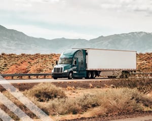 blue semi truck drives along a desert road