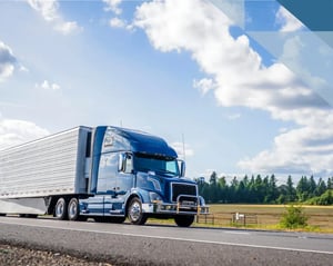 blue semi truck drives along a road with clear skies in the background